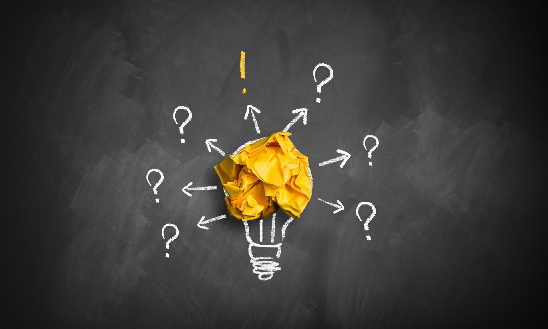 Weiße, zusammengefaltete Papierkugeln, gelbe Papierkugel mit Umriss einer Glühbirne